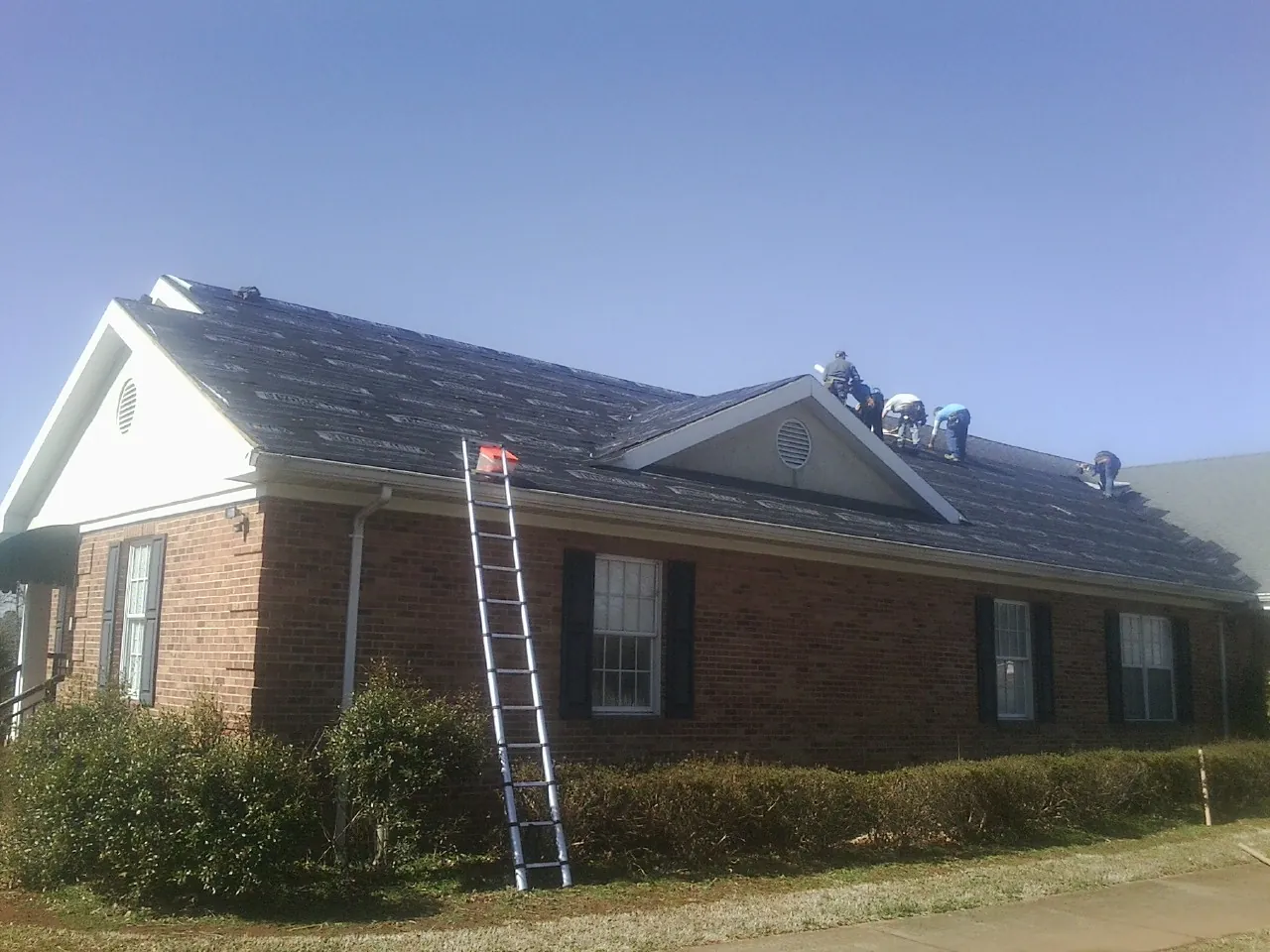 Crew tearing shingles off a brick ranch roof with a ladder set — Metal Roof Repair work by our crew in Laurel Springs