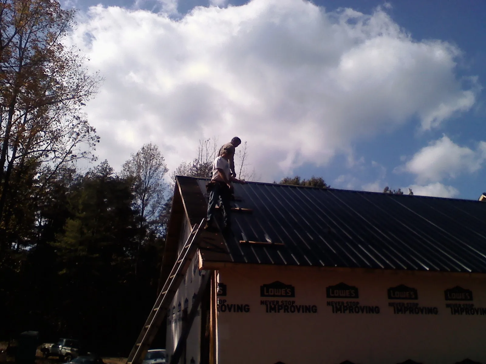 Roofer fastening dark metal panels high against a cloudy sky, from a Roof Inspection job in Laurel Springs