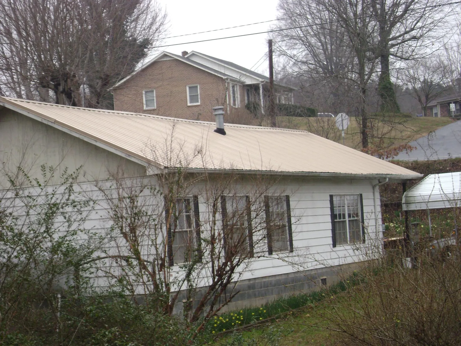 Tan metal roof on a white sided house set into a hillside — Commercial Roofing by Roofing Brothers in Laurel Springs